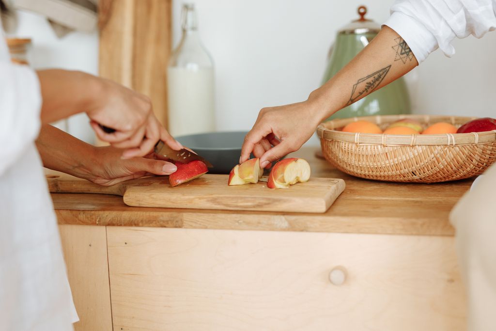 Close-up of hands cutting apples on a wooden board in a warm kitchen environment.
